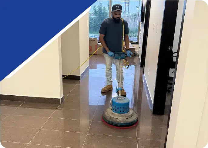A man operating a blue floor buffing machine on a shiny floor in a hallway.