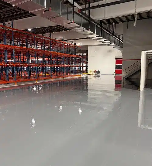 An empty warehouse interior featuring polished floors and red metal shelving units.