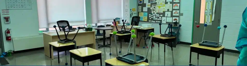 An empty school classroom with desks, chairs, and bulletin boards.