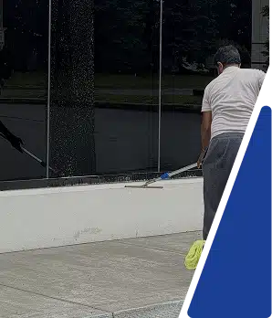 A person using a squeegee to clean large, dark-tinted exterior building windows.