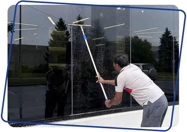 A person washing a large glass window pane from the outside using an extension pole squeegee.