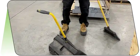 Close-up of a person's legs in work boots standing next to a yellow mop handle.