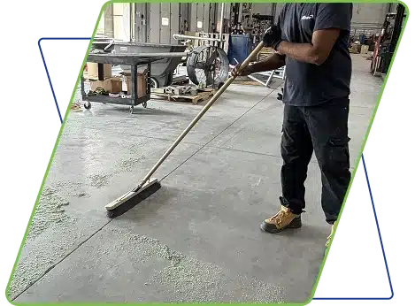 A person in a dark uniform mopping a large grey floor in an industrial space.
