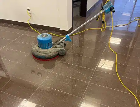 A blue floor buffing machine operating on a shiny dark brown floor.
