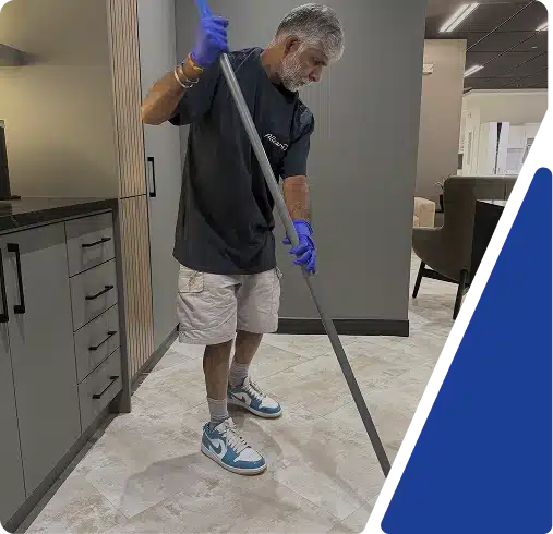 A man wearing a t-shirt and shorts mopping an office floor, framed by blue and white graphics.