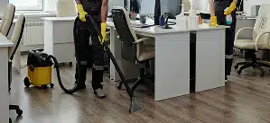 Professional office cleaning team vacuuming and sanitizing workstations