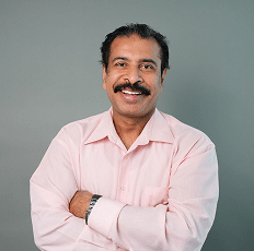 Headshot of a smiling man with a mustache wearing a light pink button-down shirt.