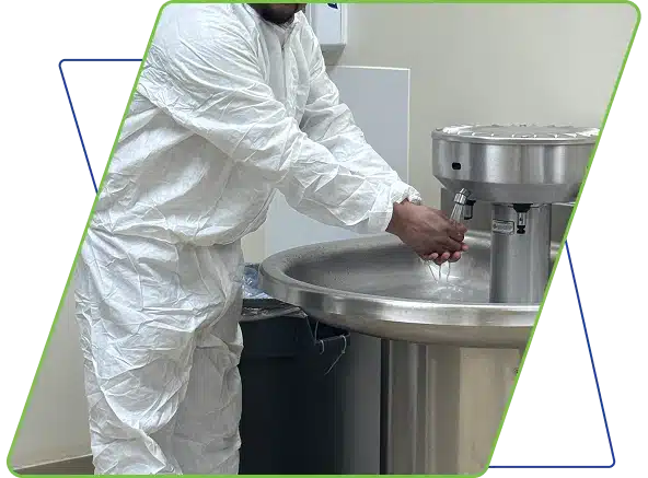 A worker in a white protective suit using a large stainless steel industrial sink, framed by a green graphic.